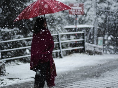 雪道を赤い傘をさして歩く女性