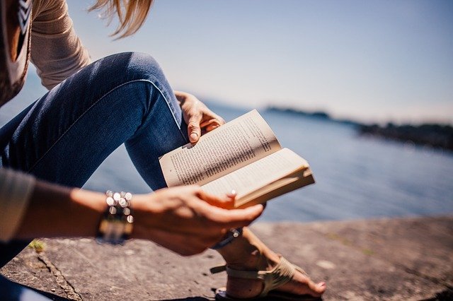 海辺に座り、本を読む女性