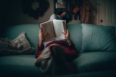 ソファに寝そべって本を読む女性