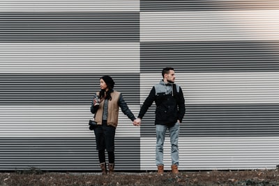 壁の前に立って手を繋いで、お互い逆方向を向き合うカップル